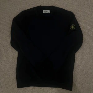 Marinblå tröja från Stone Island - Säljer en marinblå långärmad tröja från Stone Island med den klassiska loggan på vänster ärm. Enkel och stilren design som passar perfekt till många olika outfits.