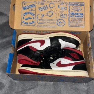 Nike Air Jordan 1 Retro Mid OG svart/röd/vit - Säljer ett par Nike Air Jordan 1 Retro High OG med klassisk färgkombination i svart, rött och vitt. Skorna har svart snörning, och röd yttersula . Perfekta för dig som gillar streetwear och sneakers med attityd. De är i hyfsat fint skick men tydligt använda. De är lite sönder bak i hälarna som man kan se på tredje bilden och sen har en av skorna en liten svart färgfläck som jag inte tror går bort (se sista bilden) priset kan diskuteras 💗