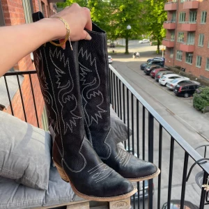 Svarta cowboy boots med vit brodyr - Säljer ett par svarta cowboy boots med vit brodyr och träfärgad klack. Skorna har spetsig tå och klassiska western-detaljer längs skaftet. Dom är så jävla snygga men säljer pga flytt. Nyskick 🤠