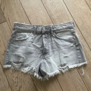 Grå jeansshorts från Zara - Säljer ett par ljusgrå jeansshorts från Zara med slitna detaljer och fransig kant nedtill. Aldrig använd prislappen är inte kvar. Midjemått 40cm
