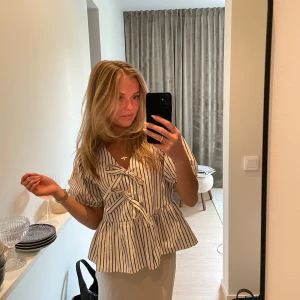 Randig blus med knyt framtill - Säljer en superfin beige blus med svarta ränder från Carin Wester i storlek 34. Blusen är använd max 5 gånger och är som i nytt skick