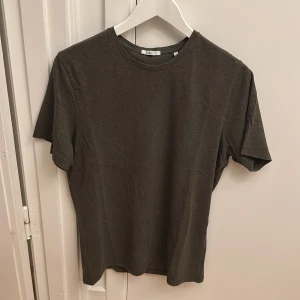 Khakifärgad T-shirt från Bläck - En basic khakifärgad T-shirt från Bläck i storlek M. T-shirten har rund halsringning och korta ärmar. Perfekt för en enkel och stilren look. Tillverkad i mjuk bomull för skön komfort.