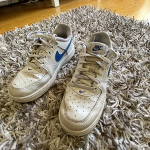 Nike Force 1 skor - Säljer ett par klassiska Nike skor med vit ovandel och blå Nike märke. 