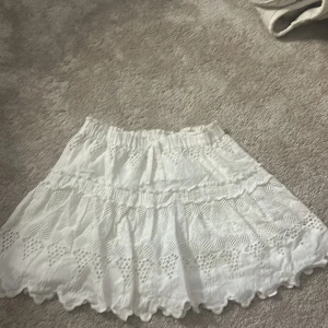 Vit volangkjol från Zara - Supersöt vit kjol från Zara med volanger och broderade spetsdetaljer. Kjolen har resår i midjan och är fodrad för extra komfort. Perfekt för sommarens alla tillfällen!