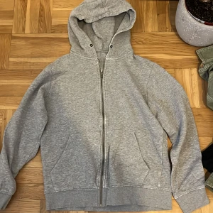 Jack&jones Grå hoodie med dragkedja - Mysig grå hoodie med dragkedja och huva. Tröjan har två stora fickor framtill och ribbade muddar vid ärmslut och nederkant. Perfekt för lager-på-lager och chill dagar.