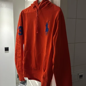 Orange hoodie från Polo Ralph Lauren - Säljer en orange hoodie från Polo Ralph Lauren med blå logga på bröstet och blå siffra 3 på ärmen. Klassisk känguruficka och justerbar huva med snören. Perfekt för en sportig och avslappnad stil. Storlek M obs sitter som en small!  Väldigt liten i storleken tillverkas inte längre köptes för 2200. Pris kan diskuteras.