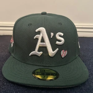 Grön keps från New Era - Mörkgrön keps från New Era med 1989 World Series-märke på sidan och MLB-logga bak. Flera broderade detaljer och platt skärm. Helt ny och oanvänd. Fraktas inom 24 timmar efter köpet🌟
