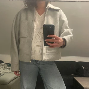 Ljusgrå från NA-KD - Säljer en ljusgrå jacka från NA-KD i ullblandning. Jackan har en rak, boxig passform med stor krage, dragkedja och en stor bröstficka. Perfekt till jeans och enkel att styla för olika tillfällen.