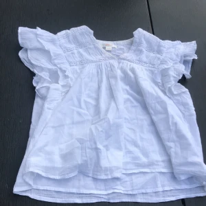 Vit blus med volang från Gina Tricot - Säljer en söt vit blus från Gina Tricot  med volangdetaljer vid axlarna och spets vid halsringningen. Blusen har en lös passform och finns både med lång ärm och ärmlös variant. Perfekt för vår och sommar! 100kr st ena av dem är inte använd tveka inte att höra av er vid frågor 🍓