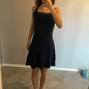 Marinblå halterneckklänning - Säljer en marinblå klänning med halterneck och tight passform upptill. Klänningen har en lätt utsvängd kjol och är ärmlös, vilket ger en stilren och enkel look. Perfekt för dig som gillar minimalistisk stil och vill ha något bekvämt men snyggt. Köpte 3 år sedan och har använt 2 gånger