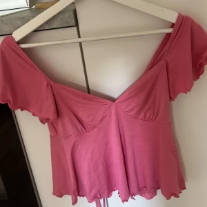 Rosa topp med volang - Säljer en söt rosa topp med volangärmar och v-ringning. Toppen har snörning i ryggen och vågig kant nertill. Perfekt för sommardagar och en trendig look!