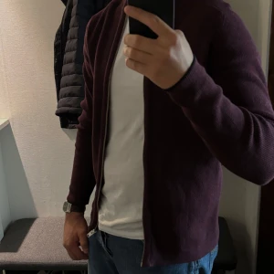 Vinröd stickad cardigan jacka från Selected Homme - Vinröd stickad cardigan jacka från Selected Homme med dragkedja framtill. Enkel och stilren design med ribbad krage och lång ärm. Perfekt för lager-på-lager och passar till jeans eller chinos.