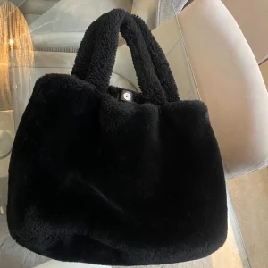 Svart fluffig handväska - Säljer en svart fluffig handväska med mjukt pälsliknande material och två rejäla handtag. Perfekt för dig som vill ha en mysig och trendig accessoar till din outfit.