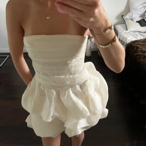 Vit kortklänning med volang - Supersöt creamvit klänning med volangkjol och markerad midja. Klänningen har en fluffig, bubblig kjol och smockad rygg för extra komfort. Perfekt för sommarens alla tillfällen! Går även att stoppa ner banden!!