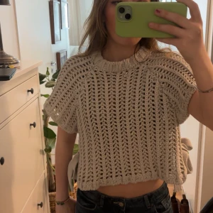 Zara topp - Säljer en beige stickad croppad tröja med korta ärmar och bred ribbad kant. Tröjan har snygga knytband i sidorna som ger en unik detalj. Perfekt för lager-på-lager och passar till både jeans och kjol.