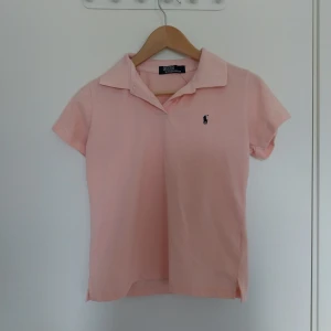 Ljusrosa pikétröja från Polo Ralph Lauren - Ljusrosa pikétröja från Polo Ralph Lauren. Har en gullig liten broderad logga på bröstet. Nästan gelt nytt skick, använts få gånger. Storlek vet jag inte, men sitter som M på mig och jag brukar ha S