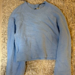 Ljusblå croppad stickad tröja - Säljer en ljusblå croppad stickad tröja med rund halsringning och långa ärmar. Tröjan har ribbade muddar vid ärmslut och nederkant, perfekt för en chill och trendig look.