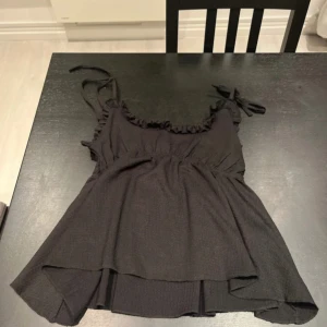 Svart linnetopp med volang och knytband från 157 - Säljer en svart linnetopp från 157 i storlek XS. Toppen har volangdetalj vid urringningen och knytband på axlarna. Perfekt för varma dagar och enkel att matcha med olika underdelar.