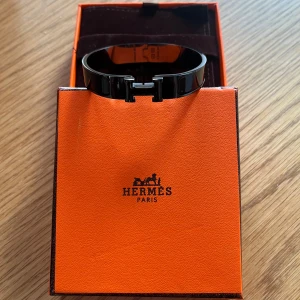 Svart armband  - Säljer ett svart armband med klassisk H-detalj, Storlek 18,5cm. Armbandet kommer i originalask och med påse, 