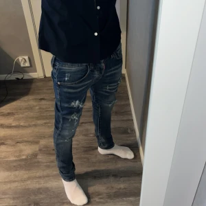Blåa dsquared2 jeans med feta slitningar - Säljer ett par blå jeans från Dsquared2 med slitningar och snygga detaljer. Jeansen har normal passform och klassisk femficksdesign. Perfekta för dig som gillar en trendig och avslappnad stil. Inga fläckar eller sådant