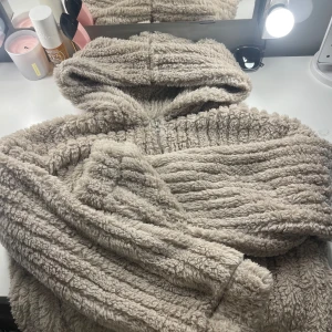 Beige teddyjacka med huva från SHEIN - Supermjuk och fluffig beige teddyjacka från SHEIN med huva och dragkedja framtill. Perfekt för kyliga dagar när du vill vara både varm och snygg. Jackan har lång ärm och är tillverkad i syntetmaterial.och har två fickor. Tröjan passar för M och mindre för den är liten i storleken 
