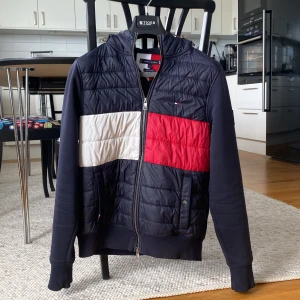 Blå quiltad jacka från Tommy Hilfiger - Säljer en snygg blå quiltad jacka från Tommy Hilfiger med dragkedja och huva. Perfekt inför sommaren! Strl S hör av dig om du har några frågor eller funderingar!