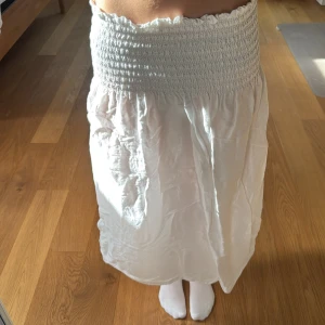 Vit långkjol med smock från Kappahl - Säljer en vit långkjol från Kappahl i storlek XS. Kjolen har bred smock i midjan som ger en bekväm passform och ett luftigt fall. Perfekt för varma dagar och enkel att styla med olika toppar.