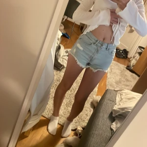 Ljusblå jeansshorts med fransar - Säljer ett par ljusblå jeansshorts med fransiga kanter och slitna detaljer. Shortsen har klassisk femficksdesign och knappgylf och i bra skick. Perfekta nu till sommaren och sjukt sköna!