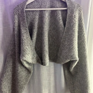 Grå croppad stickad kofta - Säljer en grå croppad stickad kofta med lång ärm. Andvänd fåtal gånger.