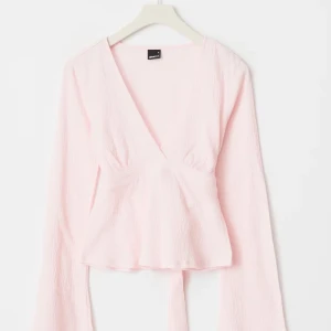 Gina topp - Säljer en ljusrosa omlottopp från Gina Tricot med lång ärm och v-ringning. Toppen har knytband i midjan. Använd ca 2 gånger. Fraktar nästan direkt!!