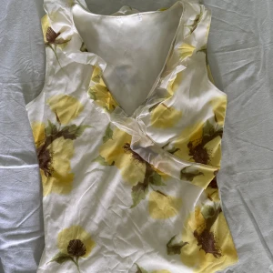 Vintage y2k Blommig ärmlös blus med volang - Säljer en söt ärmlös blus med stora gula blommor på vit botten. Blusen har v-ringning med volangdetalj längs kanten och omlottkänsla framtill. Perfekt för vår och sommar! Vintage y2k <3