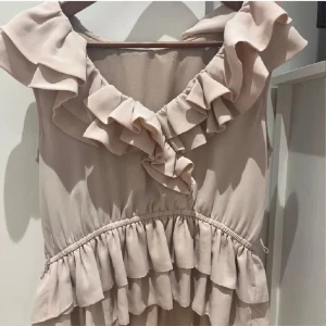 Beige volangblus med v-ringning - Supersöt beige topp med volangdetaljer och v-ringning. Blusen har ärmlös design och markerad midja med volanger både upptill och nedtill. Perfekt för sommarens alla tillfällen. Super eftertraktad och populär🥰Sitter som S.