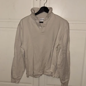 Beige långärmad tröja från East West - Säljer en stilren beige långärmad tröja från East West. Tröjan har hög krage med knappar och ribbade muddar vid ärmslut och nederkant. Aldrig använd men har legat i garderoben, därför är den skrynklig