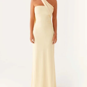 Champagnefärgad långklänning med oneshoulder - Elegant långklänning i champagnefärg med stilren oneshoulder-design och draperad detalj över axeln. Klänningen har figurnära passform och är tillverkad i ett mjukt, slätt material som ger en lyxig känsla.