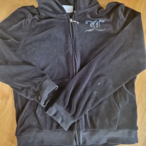 Svart velour hoodie från Juicy Couture - Mjuk svart hoodie i velour från Juicy Couture med glittrande stenar på bröstet och stor Juicy Couture-logga på ryggen. Dragkedja framtill, huva och långa ärmar. Perfekt för en avslappnad och trendig look. Storlek 15/16, men skulle säga xs/s. Använt skick, men fullt brukar, därav priset.