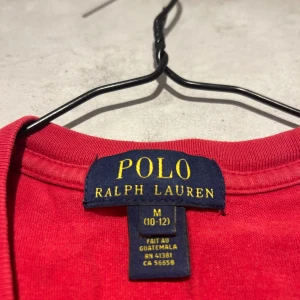 Röd t-shirt från Polo Ralph Lauren - Säljer en klassisk röd t-shirt från Polo Ralph Lauren med broderad svart logga på bröstet. T-shirten har rund halsringning och korta ärmar. Perfekt för en stilren och enkel look. Storlek 10-12 år