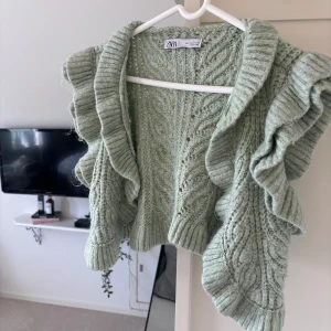Ljusgrön stickad kofta från Zara - Superfin ljusgrön stickad kofta från Zara med volangdetaljer längs ärmarna och framkanten. Kortare modell som passar perfekt till både jeans och klänning. 