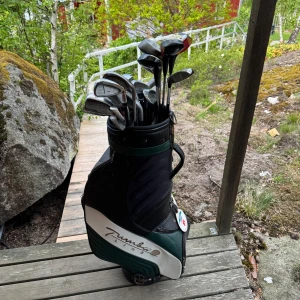 Svart och vit golfbag med klubbor - Golfbag i svart och vitt med flera olika golfklubbor, bland annat från märkena Ping och Maggo. Bagen har handtag och flera fack, perfekt för att ta med till golfbanan. Snygg och praktisk design. Det är totalt 32 klubbor