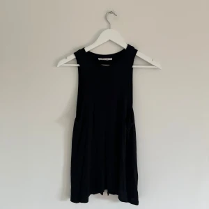 Svart ärmlös linnetopp från Gina Tricot - En svart ärmlös linnetopp från Gina Tricot med rund halsringning. Toppen har en enkel och stilren design i mjukt material, perfekt för varma dagar eller som lager under andra plagg. Öppen i ryggen 