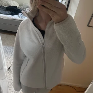 Vit fleecejacka med dragkedja - Mysig vit fleecejacka med hög krage och hel dragkedja framtill. Jackan har två sidofickor med dragkedja och en enkel, stilren design. Perfekt för kyliga dagar och enkel att matcha med olika outfits. PRIS GÅR ATT DISKUTERA!!