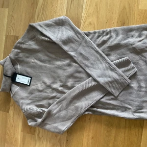 Beige ribbad tröja med polokrage - Säljer en beige ribbad tröja med lång ärm och polokrage. Tröjan har en tight passform och är tillverkad i ett mjukt, stretchigt material som sitter snyggt på kroppen. Perfekt för dig som gillar stilrena och enkla plagg.