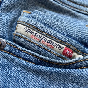 Blå jeans från Diesel, W29 L 32 - Säljer ett par klassiska blå jeans från Diesel med raka ben och snygga detaljer. Jeansen har fem fickor, tydliga sömmar och en liten logotyp på bakfickan. Perfekta för dig som gillar stilrena och tidlösa jeans. Jeansen är knappt använda och är i fint skick. Det finns även inga tecken på användning.
