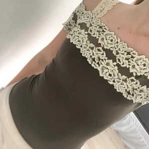 Brun bodysuit med spetsdetaljer från Intimissimi - Supersnygg brun bodysuit från Intimissimi med breda axelband och dekorativa spetsdetaljer i offwhite längs halsringningen. Stretchigt material som sitter tight och markerar figuren. Perfekt att styla till både jeans och kjol. Stolek S!