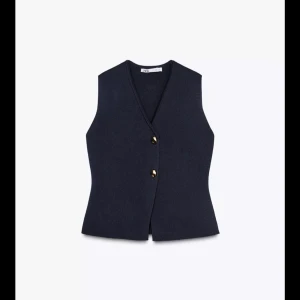 Mörkblå väst med knappar - Snygg mörkblå väst från Zara med två dekorativa knappar framtill och v-ringad hals. Västen har en figurnära passform och är perfekt att styla över en skjorta eller t-shirt. Enkel och stilren design som passar till många outfits.
