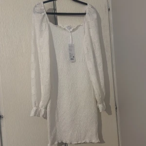 Vit klänning med puffärmar och spetsdetaljer - Superfin vit klänning med långa puffärmar i spets och smockad kropp. Fyrkantig ringning och lätt volang vid ärmslut. Perfekt för sommarens tillfällen eller studentfirande. Har aldrig använt den prislappen är på köpte fel storlek ❤️