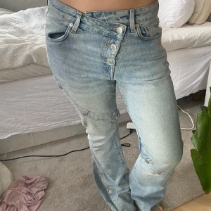 Ljusblå jeansbyxor med knappar - Säljer ett par ljusblå jeansbyxor med flera synliga knappar framtill och längs bennen. Dom är väldigt unika, inte alls använda mkt!