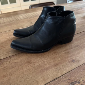 Svarta boots med stjärndetalj - Säljer ett par svarta boots i skinn med spetsig tå och dragkedja på sidan. På baksidan finns en vit stjärna som snygg detalj. Perfekta för dig som vill sticka ut lite extra med dina skor. Köpta på Mathilde i PK-huset. 