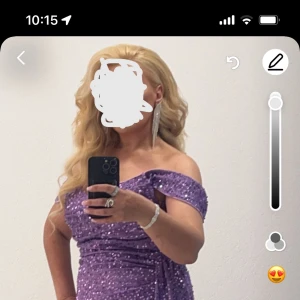 Lila glittrig långklänning med slits - Säljer en lila långklänning med glittriga paljetter och offshoulder-design. Klänningen har en hög slits framtill och markerad midja, perfekt för bal eller fest. Materialet är syntet och den har en elegant, figurnära passform.