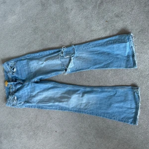 Ljusblå slitna bootcut jeans - Säljer ett par ljusblå jeans med bootcut passform och slitna detaljer på låret
