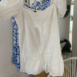 Vit klänning med broderade blommor - Söt vit klänning med puffärmar och broderade blommor. Klänningen har volang nertill och är tillverkad i ett lätt bomullstyg. Perfekt för varma dagar och har en romantisk känsla med sina fina detaljer.
